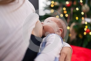 Mother and son breastfeeding baby sitting on sofa by christmas tree at home