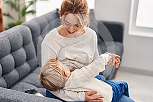 Mother and son breastfeeding kid sitting on sofa at home