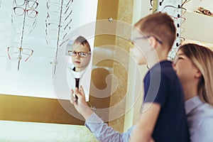 Mother with son choosing glasses in optics store.