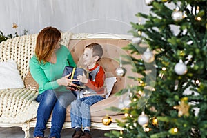 A mother and a son with christmas presents in front of the fur-tree with candles.