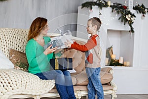 A mother and a son with christmas presents in front of the fur-tree with candles.