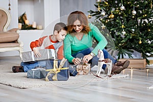 A mother and a son with christmas presents in front of the fur-tree with candles.