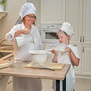 Mother and son cooking apple pie in the home kitchen. A woman and a boy in chef hats and aprons cook with pastries