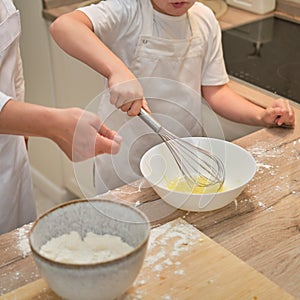 Mother and son cooking apple pie in the home kitchen. A woman and a boy in chef hats and aprons cook with pastries