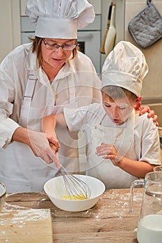 Mother and son cooking apple pie in the home kitchen. A woman and a boy in chef hats and aprons cook with pastries