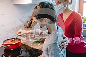 Mother and son cooking at home together wearing masks