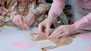 Mother and son are cutting parts for gingerbread house from dough hands closeup.