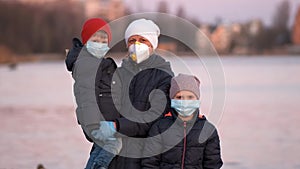 Mother, son and daughter in medical masks on the lake in the Park. Protection against coronavirus infections Covid-19