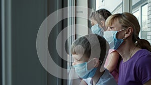 Mother, son and daughter in medical masks near the window in isolation for virus outbreak . The concept of protection against