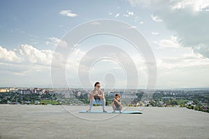 Mother and son doing exercise on the balcony in the background of a city during sunrise or sunset, concept of a healthy