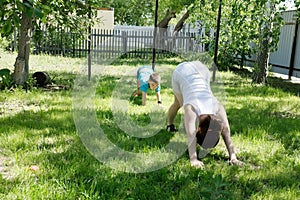 Mother and son doing yoga exercises on grass in the yard at the day time. People having fun outdoors
