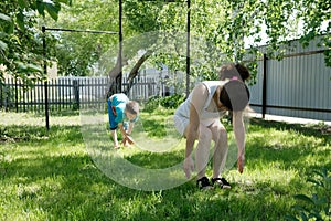 Mother and son doing yoga exercises on grass in the yard at the day time. People having fun outdoors