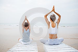 A mother and a son are doing yoga exercises at the seashore of t