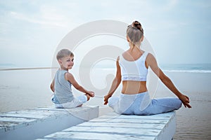 A mother and a son are doing yoga exercises at the seashore of t