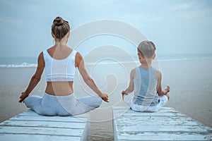 A mother and a son are doing yoga exercises at the seashore of tropic ocean