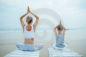 A mother and a son are doing yoga exercises at the seashore of tropic ocean