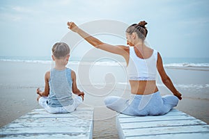 A mother and a son are doing yoga exercises at the seashore of tropic ocean