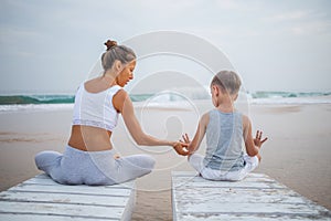 A mother and a son are doing yoga exercises at the seashore of tropic ocean