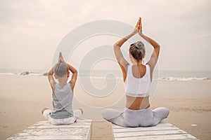 A mother and a son are doing yoga exercises at the seashore of tropic ocean