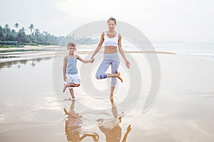 A mother and a son are doing yoga exercises at the seashore of tropic ocean