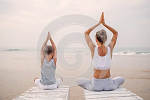 A mother and a son are doing yoga exercises at the seashore of tropic ocean