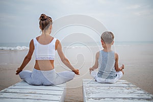 A mother and a son are doing yoga exercises at the seashore of tropic ocean