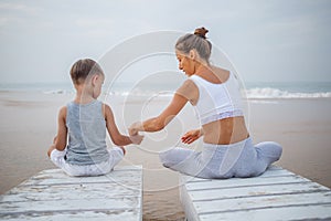 A mother and a son are doing yoga exercises at the seashore of tropic ocean