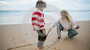 Mother son drawing beach with sticks on autumn weekend. Family playing seaside