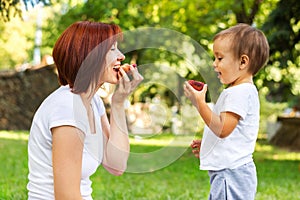 Mother and son eating peach on a picnic in the park. Mom and son sharing one fruit outdoor. Healthy parenting concept