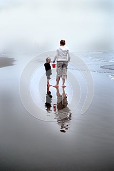 Mother and Son on Foggy Beach with Red Bucket Pail
