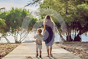 Mother and son go to the sea beach. Resort vacation on tropical beach. Path to beach