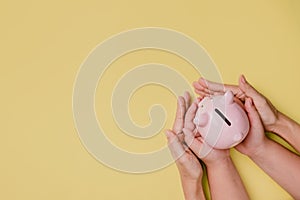 Mother and son hand holding piggy bank on yellow background