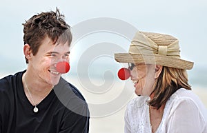 Mother and son having fun laughing celebrating red nose day on beautiful beach holiday