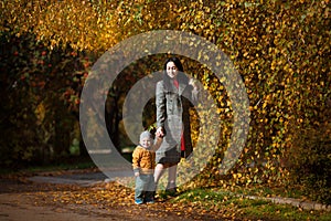Mother and son having fun together in autumn park. Happy family walking in yellow trees in fall. Thanksgiving holiday