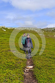 Mother and son hiking in tundra mountains on path surrounded with lingonberry bushes Sweden