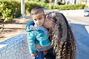 Mother and son hugging each other and kissing sitting on bench at park