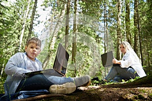Mother and son with a laptops in forest in summer. Fat young smart teenage boy and woman working with modern IT
