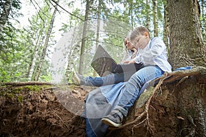 Mother and son with a laptops in forest in summer. Fat young smart teenage boy and woman working with modern IT