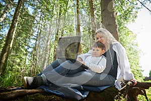 Mother and son with a laptops in forest in summer. Fat young smart teenage boy and woman working with modern IT