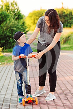 Mother and son learning to ride scooter. Childhood. Happy holidays with parents