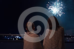 Mother and son looking at New Year celebration fireworks in night sky warmly wrapped in striped plaids standing on home balcony