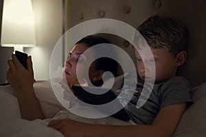Mother with son looks in their electronic devices lying in bed