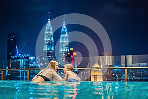Mother and son in outdoor swimming pool with city view at night