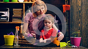 Mother with son plant flowers in colored pots. Happy family spending time together. Happy summer day.