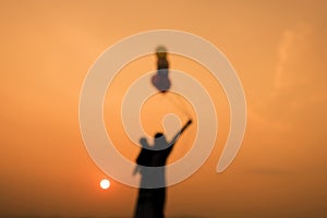 Mother and son play balloon silhouette at sunset,blur background