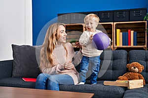 Mother and son playing with ball sitting on sofa at home