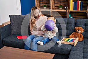 Mother and son playing with ball sitting on sofa at home