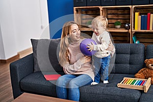 Mother and son playing with ball sitting on sofa at home