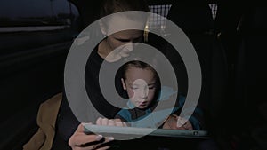 Mother and son playing with touch pad during night car ride