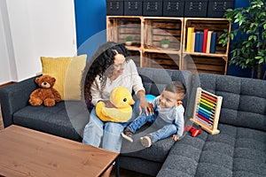 Mother and son playing with toys sitting on sofa at home